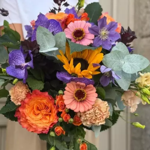 Bouquet de saison aux roses orange, zinnias corail, tournesol et orchidées vanda violettes