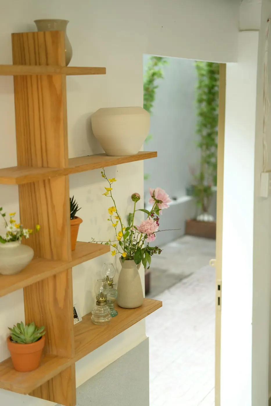 Étagère en bois clair garnie de vases en céramique, de plantes grasses et de petits bouquets champêtres