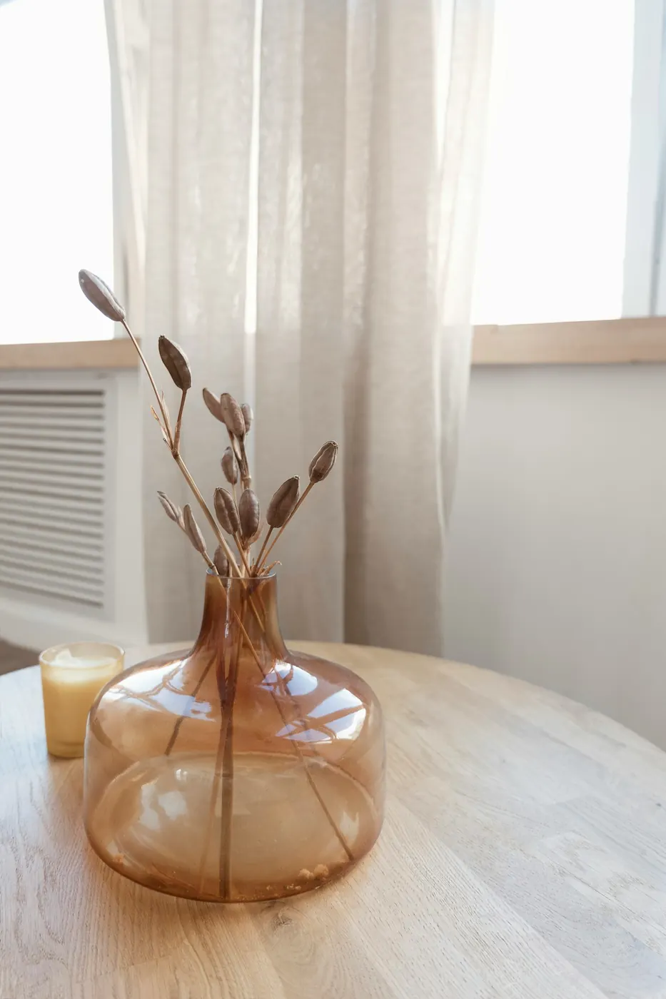 Fleurs séchées dans un vase en verre ambré, posé sur une table en bois près d’une fenêtre