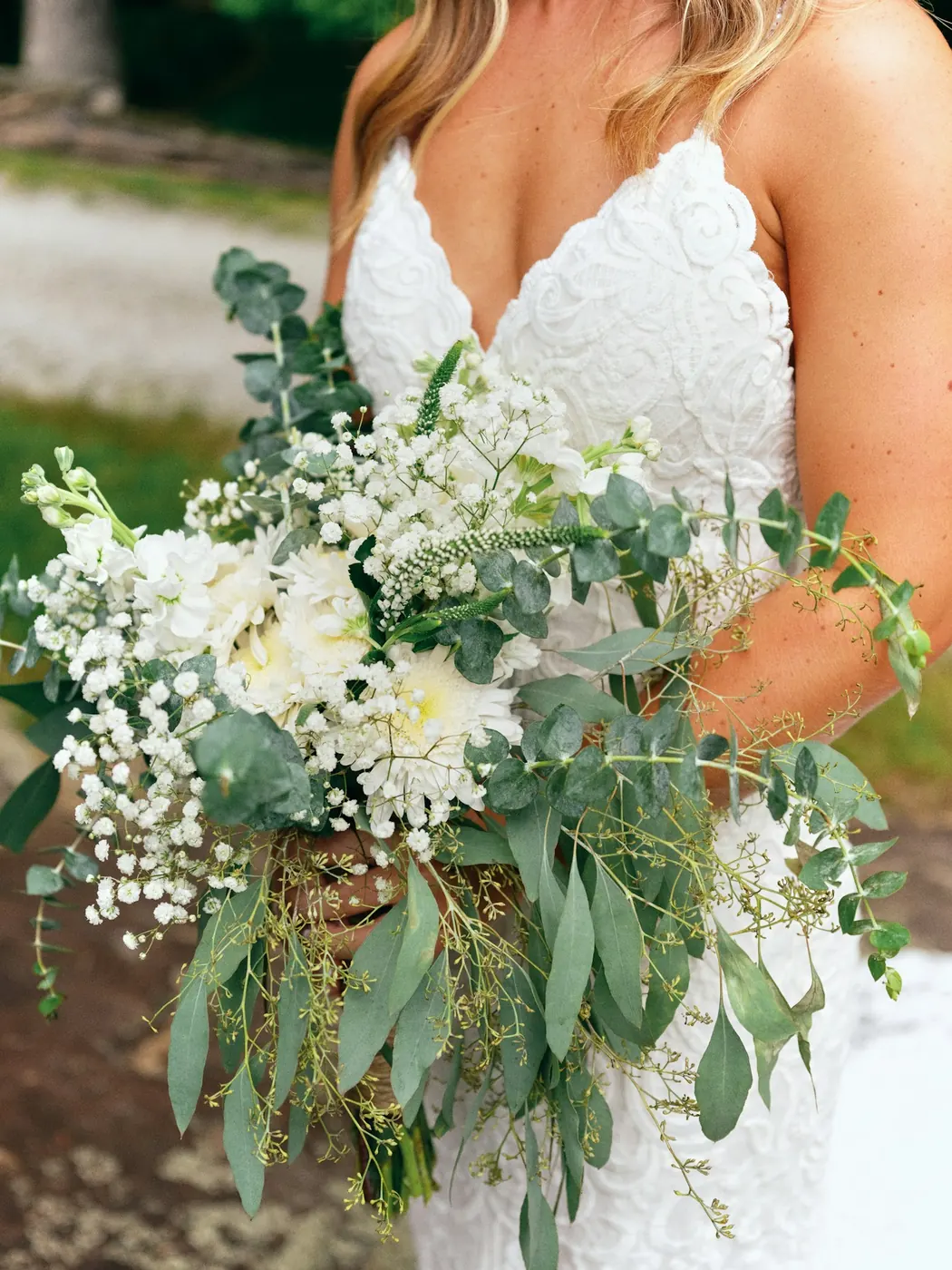 Mariée en robe de dentelle tenant un bouquet de gypsophile, de fleurs blanches et de branches d’eucalyptus